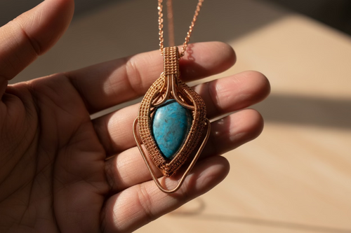 Azure Ember Talisman resting in hand, showcasing intricate copper weaving and a vivid blue stone.