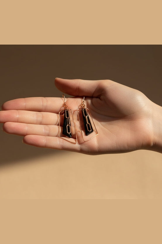 Hand holding two pairs of earrings against a beige background