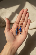 Close-up of handcrafted copper wire wrapped earrings with blue gemstone chips and faceted blue chalcedony beads held in hand.