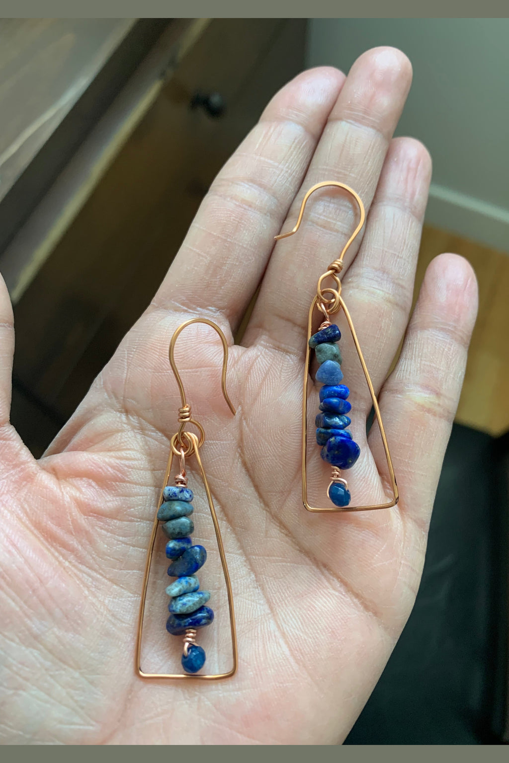 Close-up of handcrafted copper wire wrapped earrings with blue gemstone chips and faceted blue chalcedony beads held in hand.