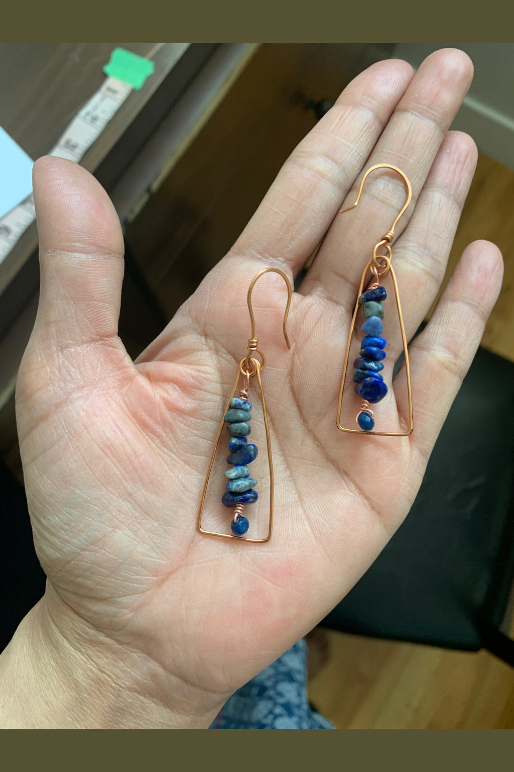 Close-up of handcrafted copper wire wrapped earrings with blue gemstone chips and faceted blue chalcedony beads held in hand.
