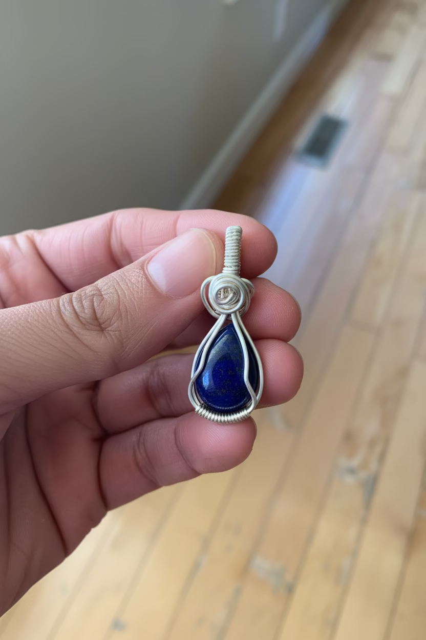 Hand holding a blue teardrop pendant with wire wrapping