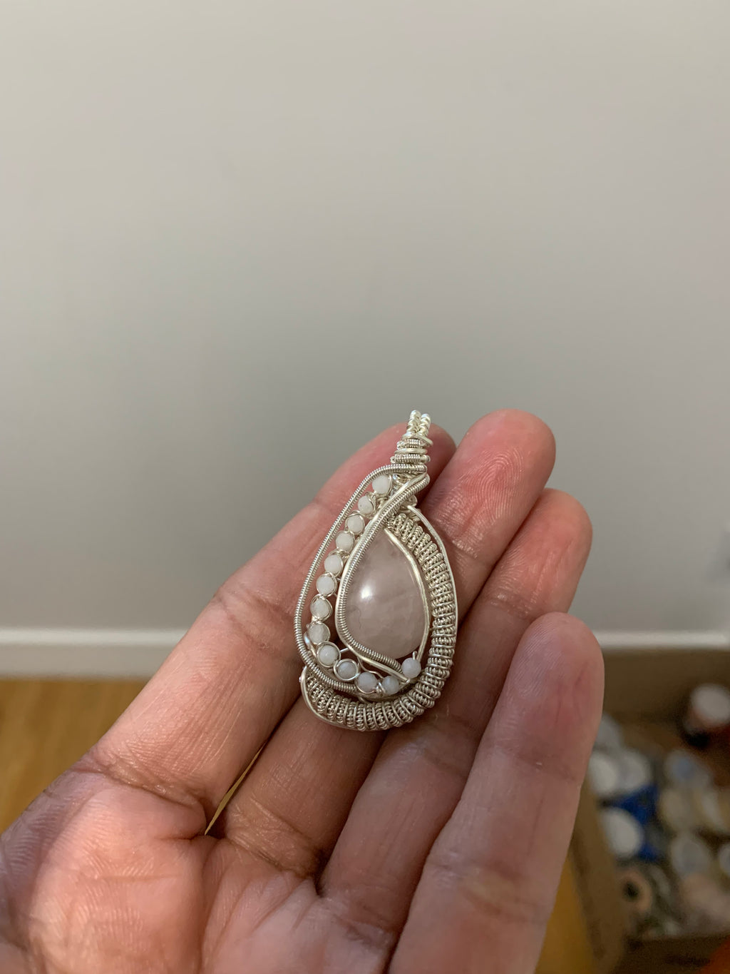 Close-up of the handcrafted Blushing Moon Pendant resting in a hand, showcasing natural Rose Quartz, Moonstones, and intricate silver-toned copper wire weaving.