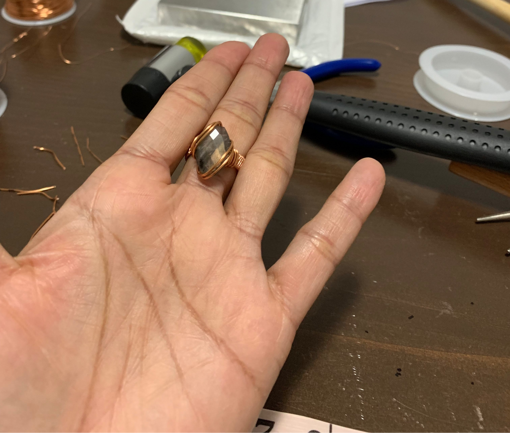 Faceted labradorite ring standing on a stone display, showing the copper wire setting and woven band.