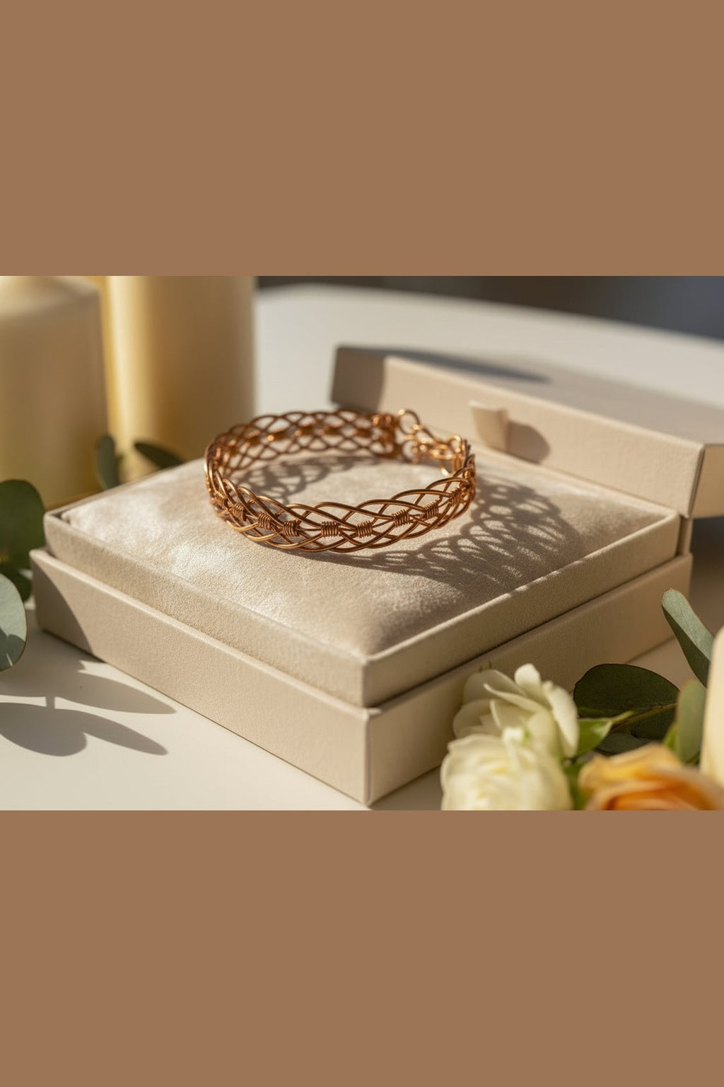 Woven copper bracelet on a beige jewelry box with flowers in the background
