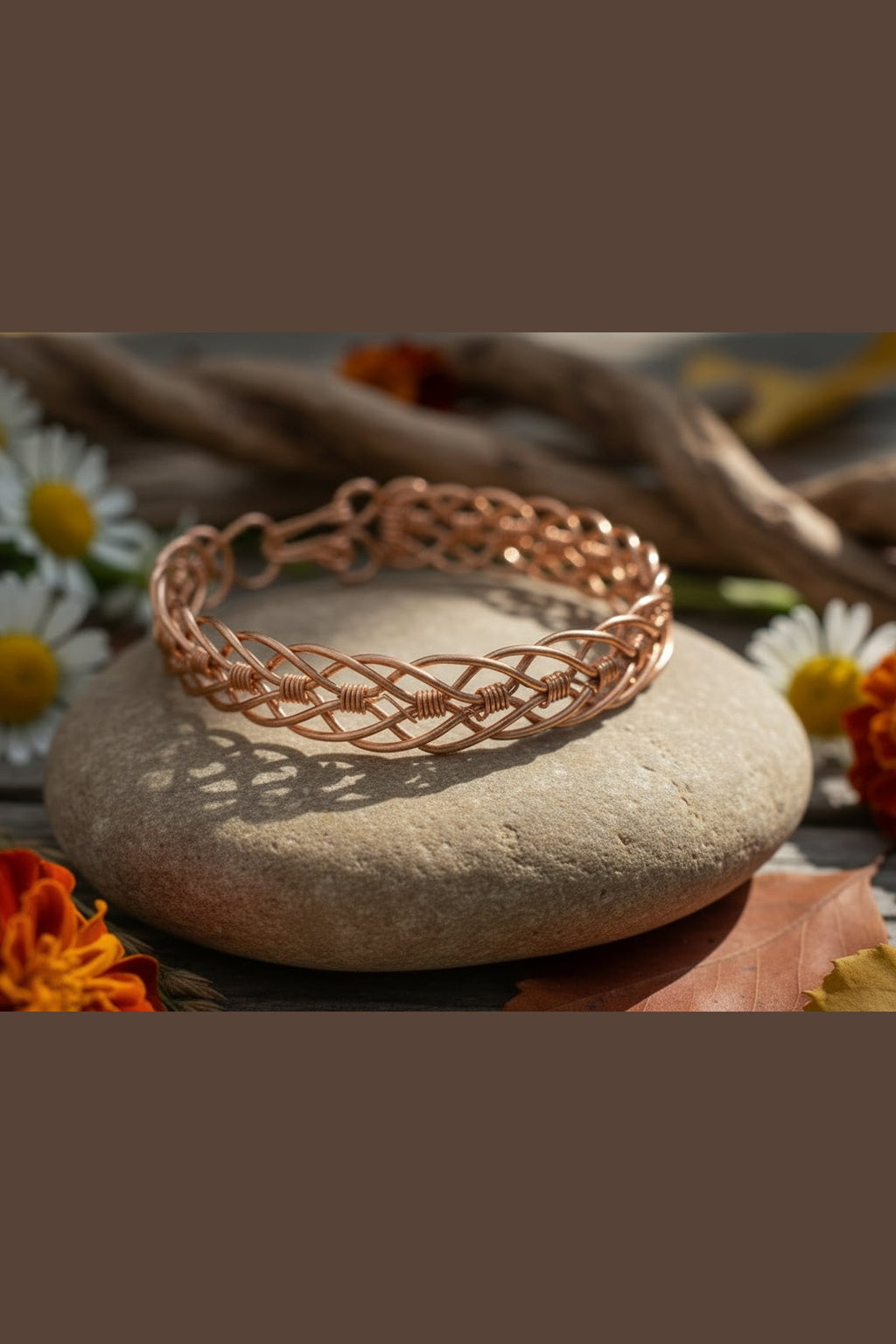Copper braided bracelet on a stone with flowers in the background