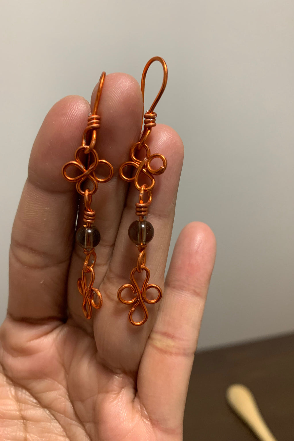 Orange wire earrings held in a hand against a neutral background