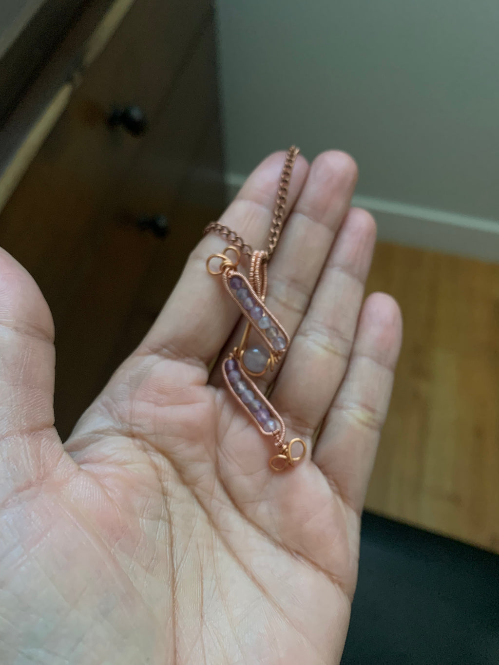 Close-up of the handcrafted Evening Lilac pendant resting in hand, featuring fourteen genuine amethyst beads and a violet center bead wrapped in warm copper wire.