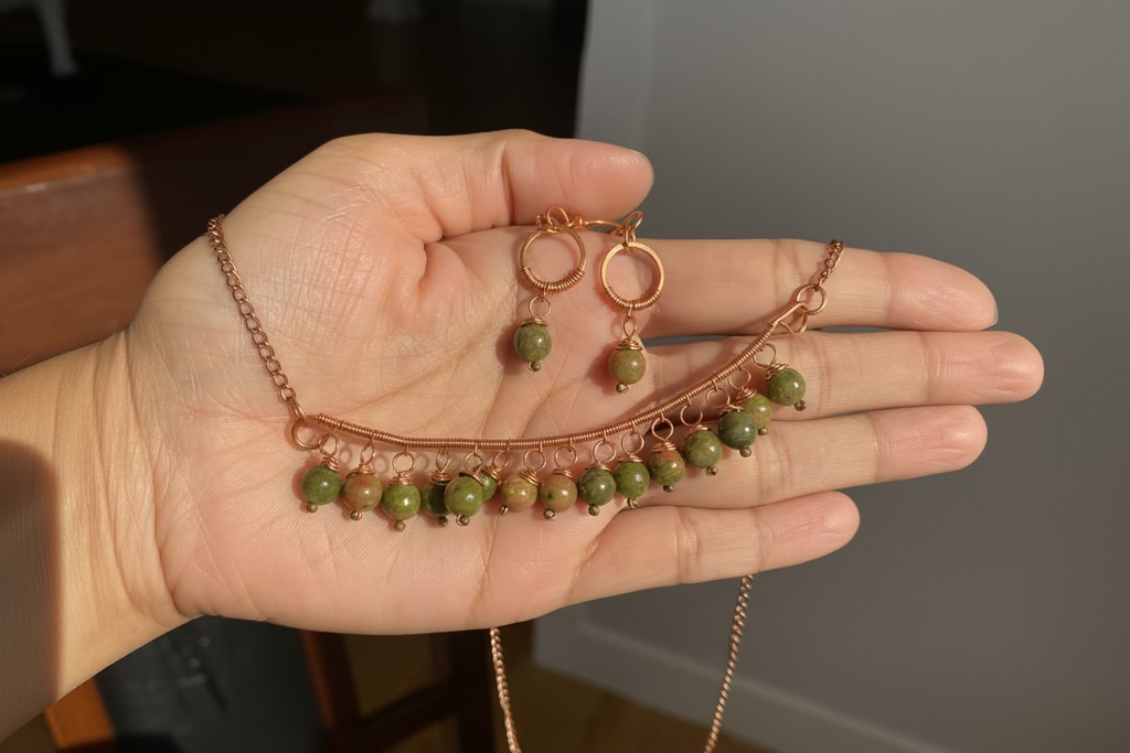 Hand holding the Evergreen Grace unakite and copper necklace, highlighting the handcrafted copper wirework and natural gemstone beads.