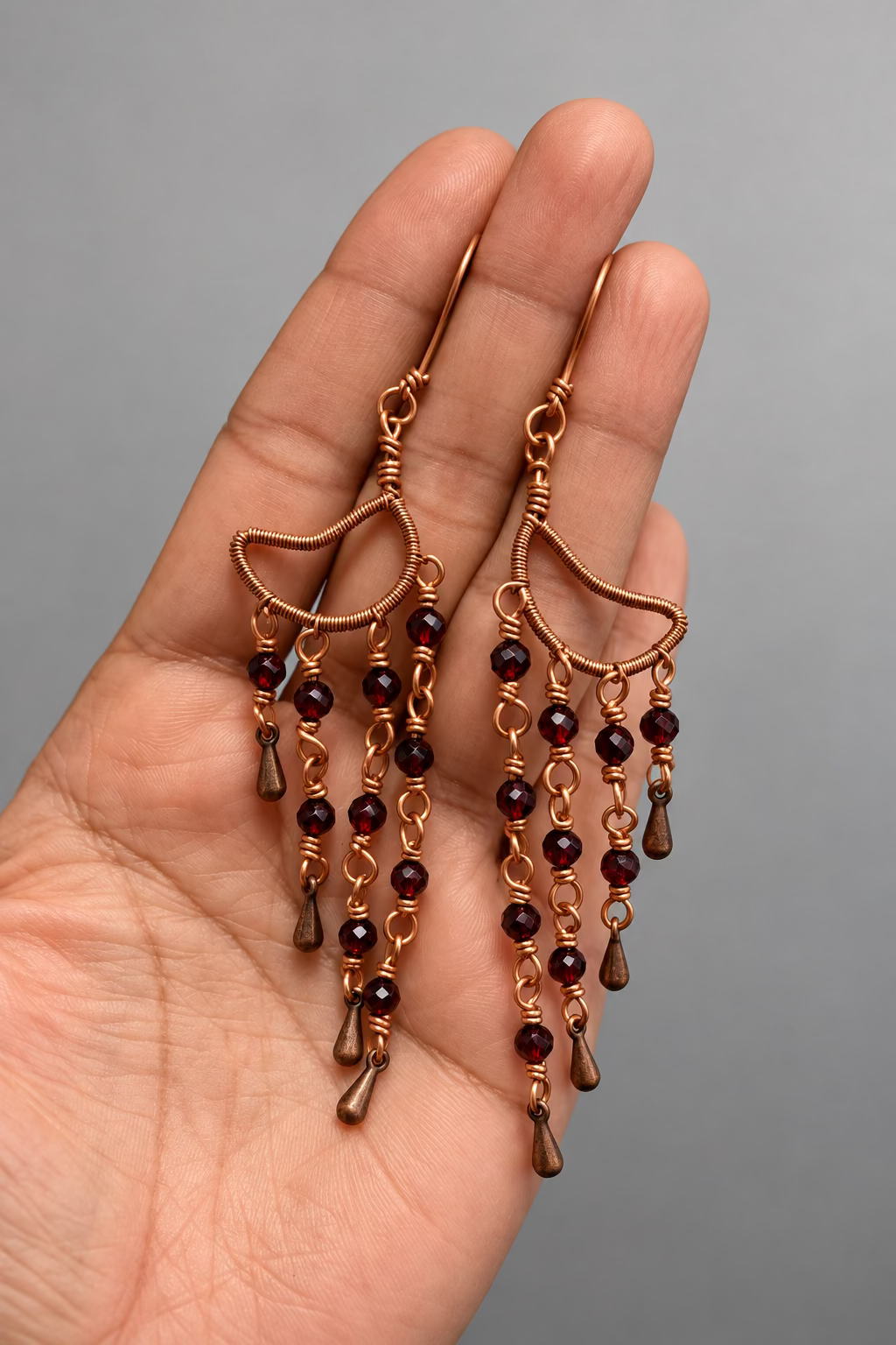 Close-up of a Garnet Alchemy Cascade Earring showing faceted red garnet beads, detailed copper wire wrapping, and cascading copper accents.