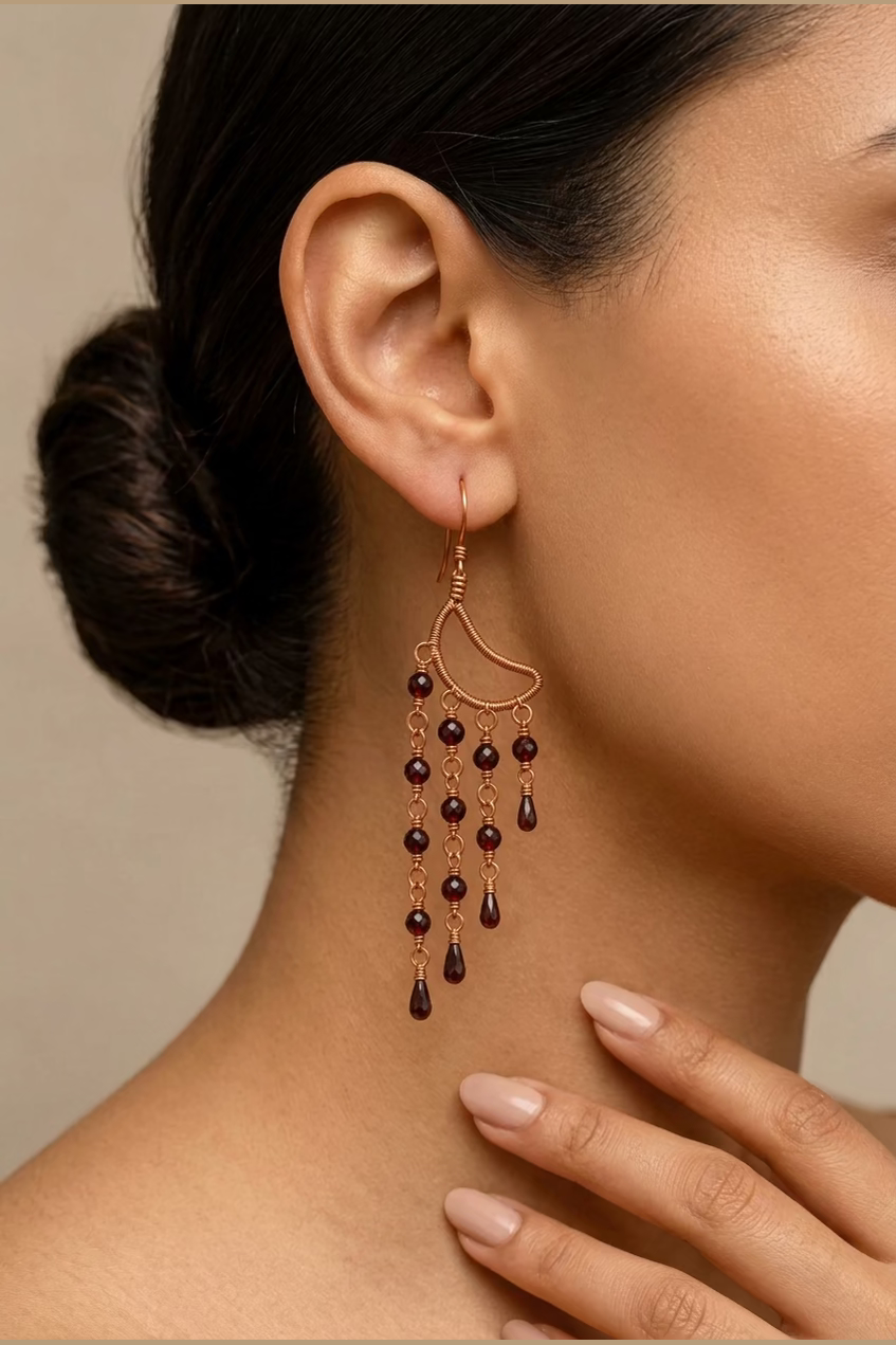 Close-up of a Garnet Alchemy Cascade Earring showing faceted red garnet beads, detailed copper wire wrapping, and cascading copper accents.
