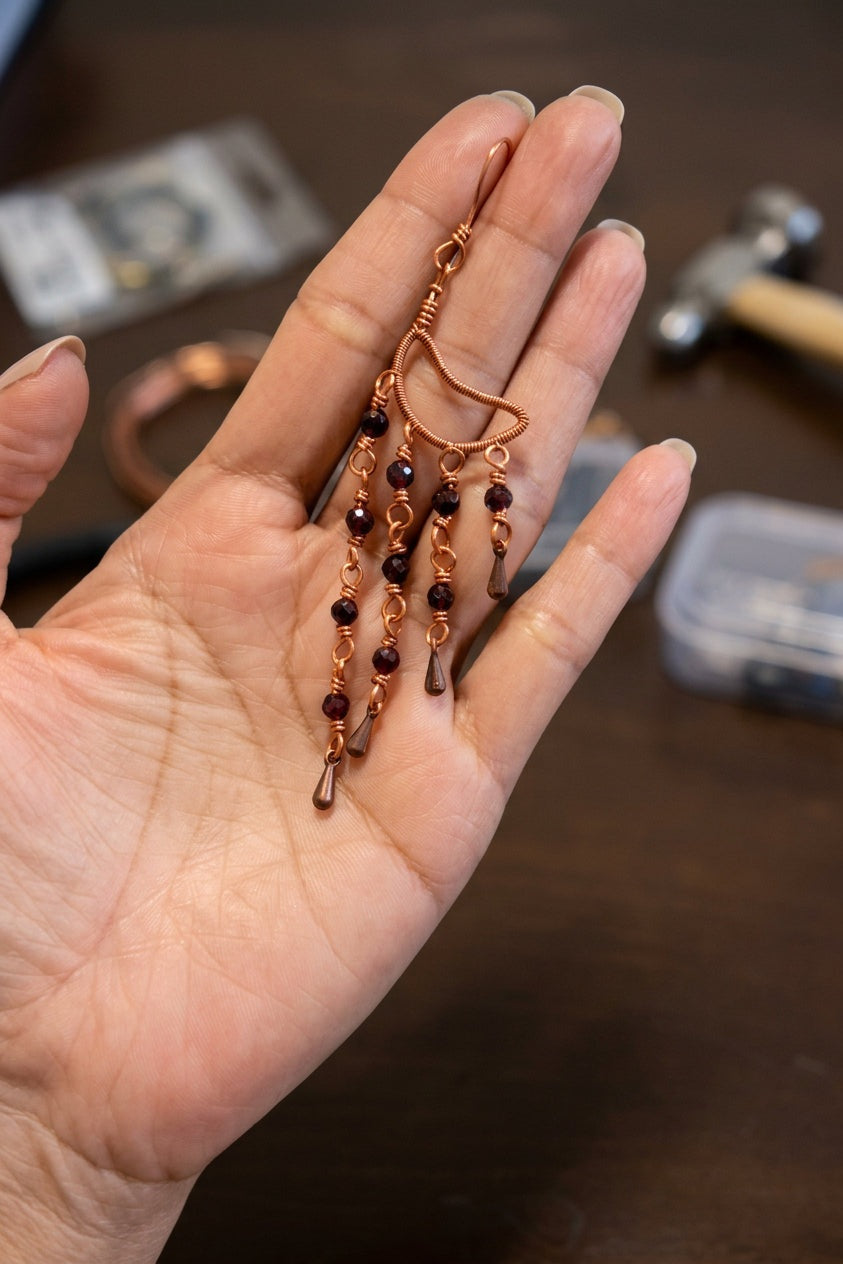 Close-up of a Garnet Alchemy Cascade Earring showing faceted red garnet beads, detailed copper wire wrapping, and cascading copper accents.