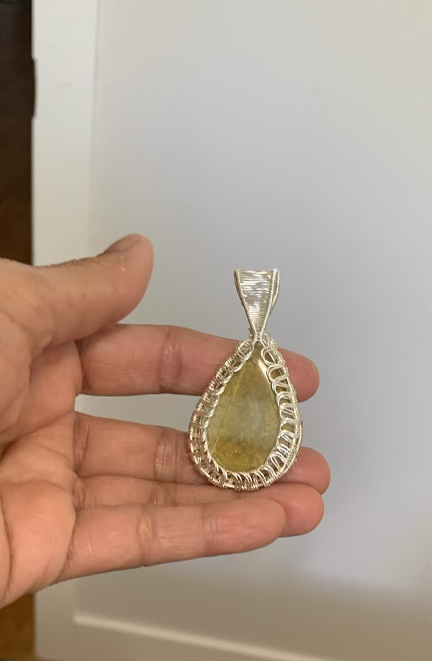 Golden resin teardrop pendant wrapped in silver wire held in hand.