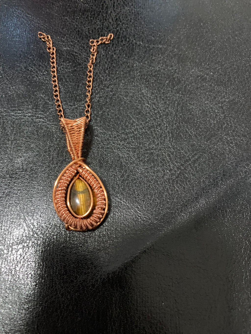 Golden Vigil handcrafted Tiger's Eye copper pendant displayed beside a candle and wooden jewellery box, highlighting its warm artisan craftsmanship.