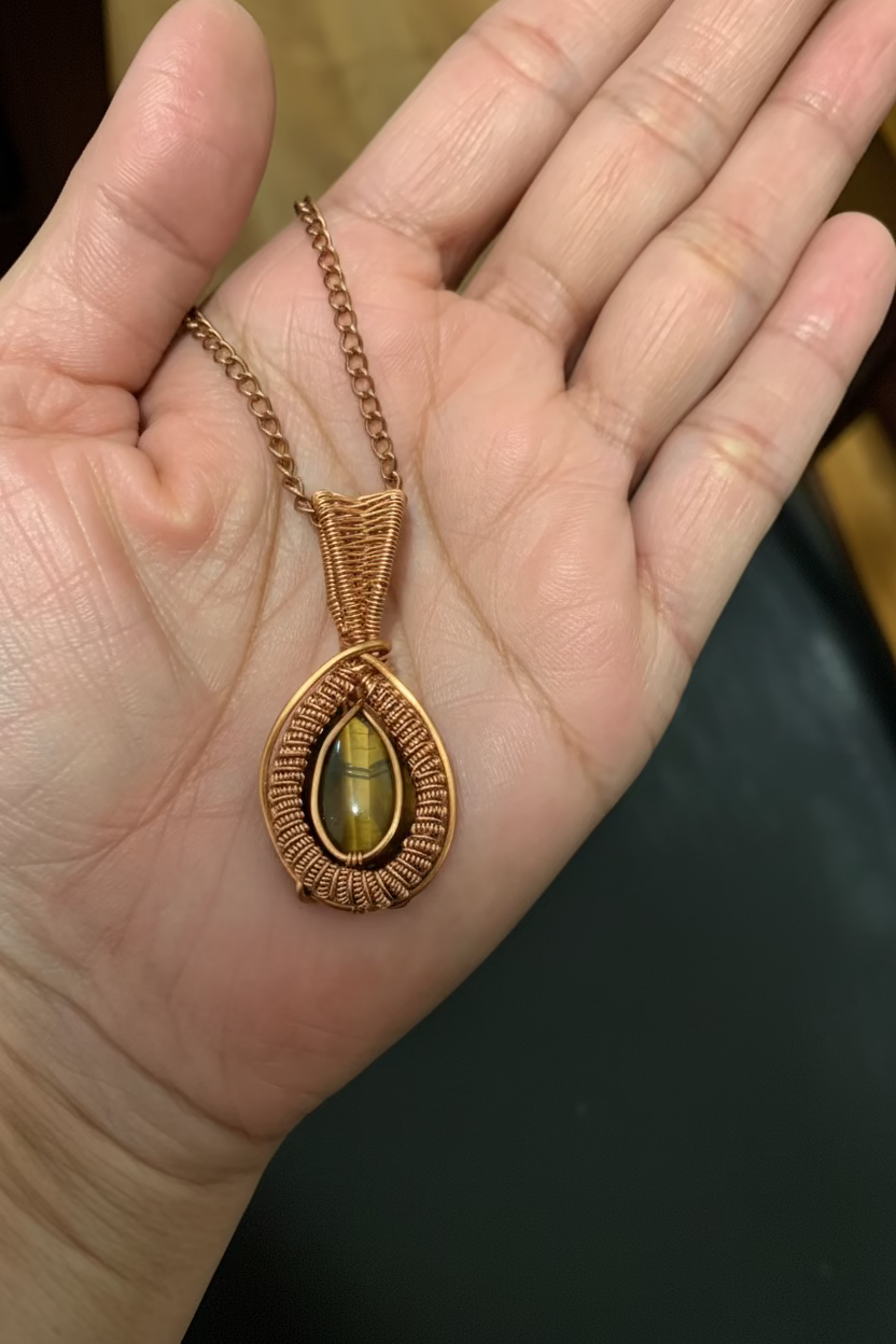 Hand holding the handcrafted Golden Vigil Tiger's Eye pendant, showcasing intricate copper wire weaving and the gemstone's golden chatoyancy.