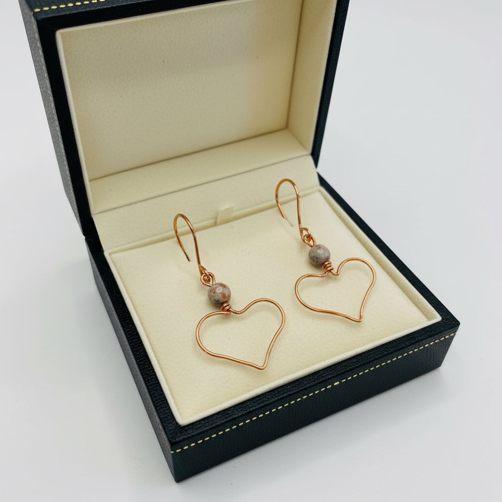 Pair of heart-shaped copper earrings with a central bead on a light background