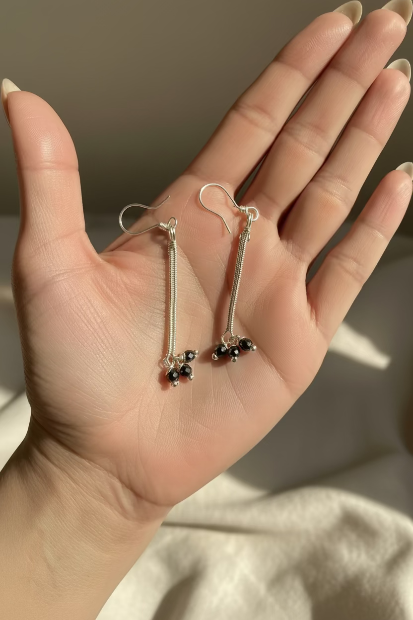 Hand holding a pair of handcrafted Hematite Stardust Earrings made with faceted hematite and silver-toned copper wire, showing the intricate wire wrapping and overall size.