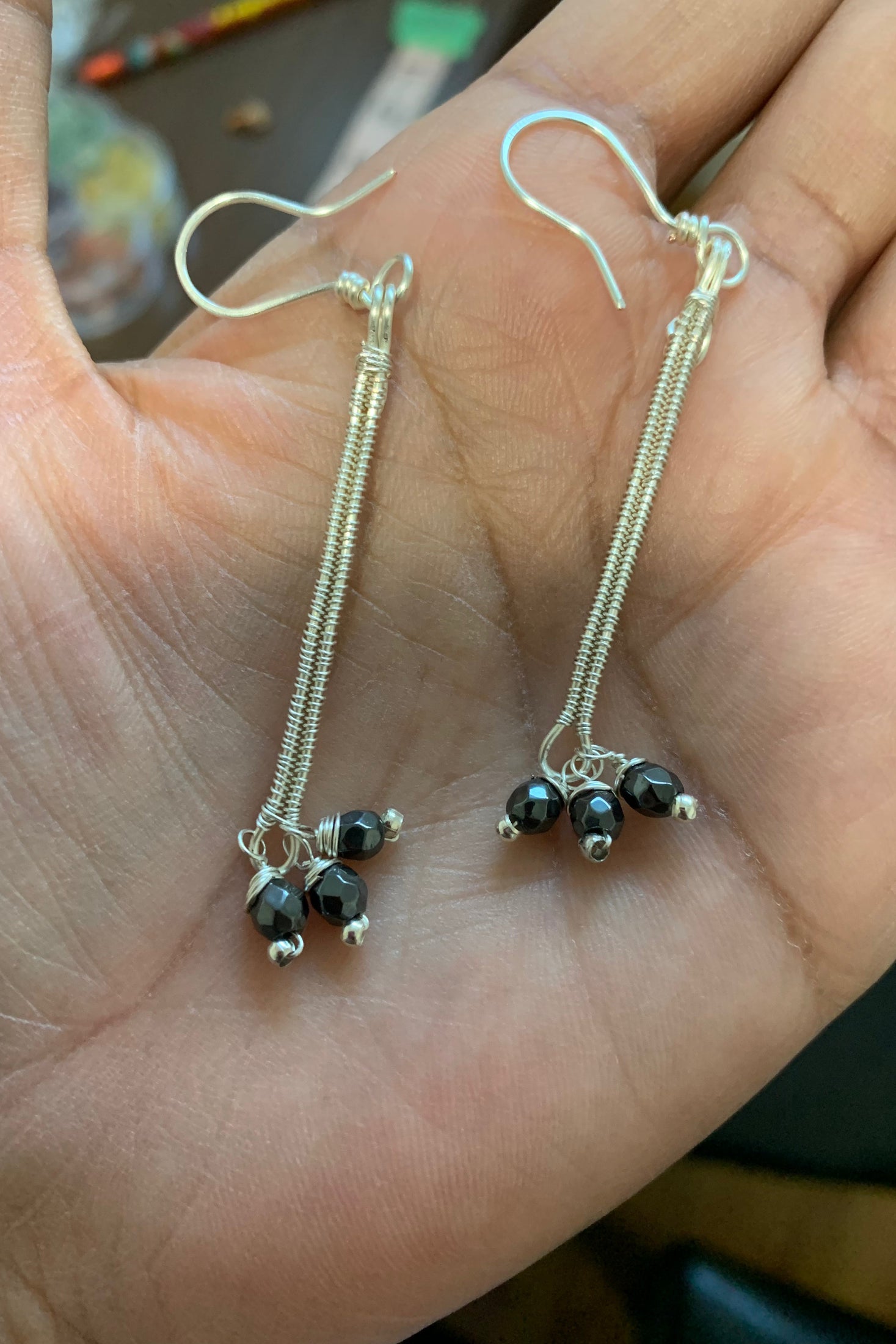 Hand holding a pair of handcrafted Hematite Stardust Earrings made with faceted hematite and silver-toned copper wire, showing the intricate wire wrapping and overall size.