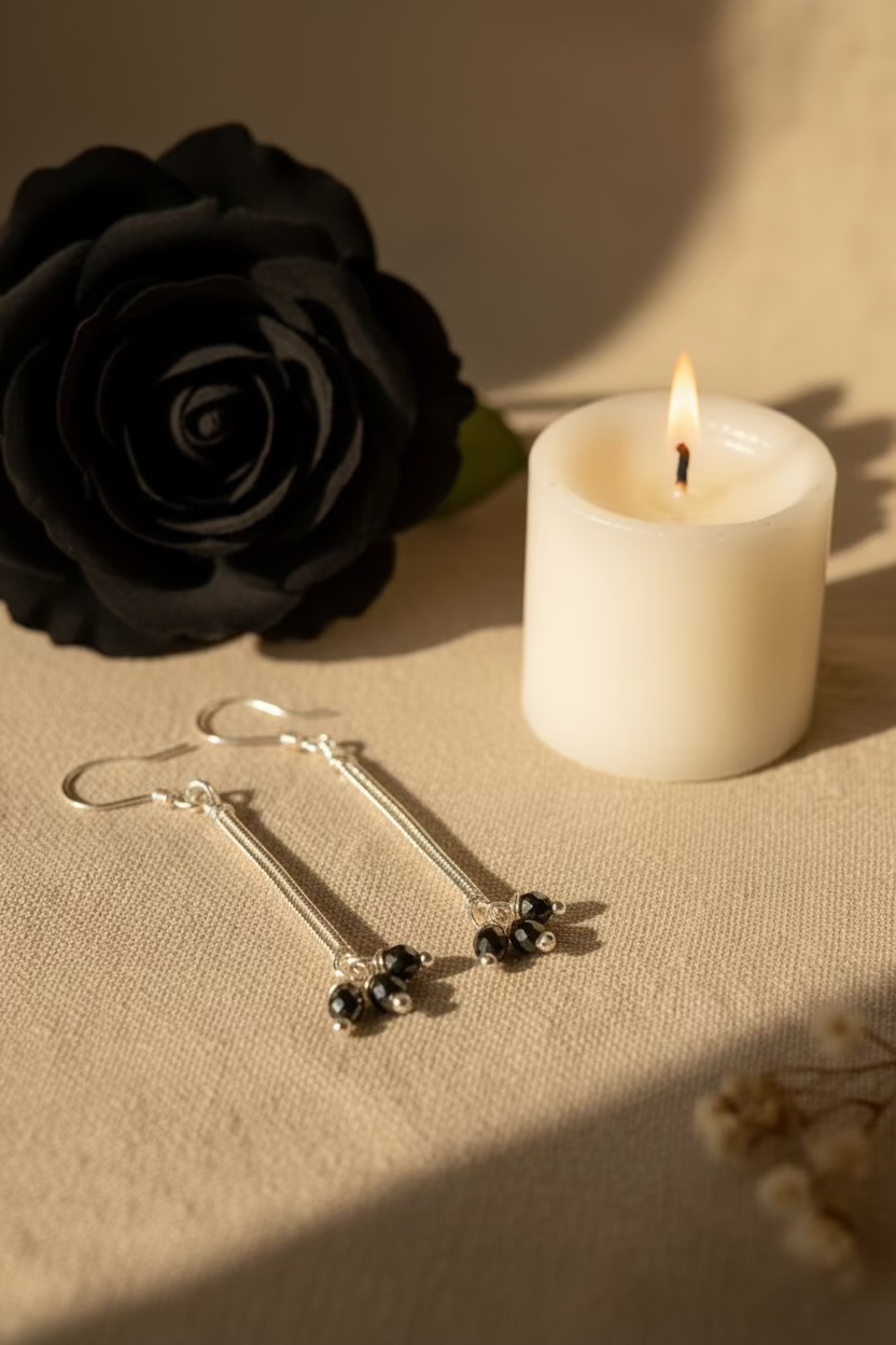 Handmade Hematite Stardust Earrings featuring faceted hematite beads wrapped in silver-toned copper wire, displayed beside a black rose and candle on a neutral fabric background.
