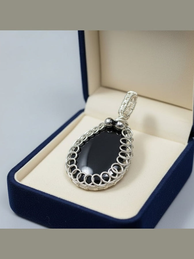 Black resin teardrop pendant with silver-toned wire detailing displayed on an elegant gift box.
