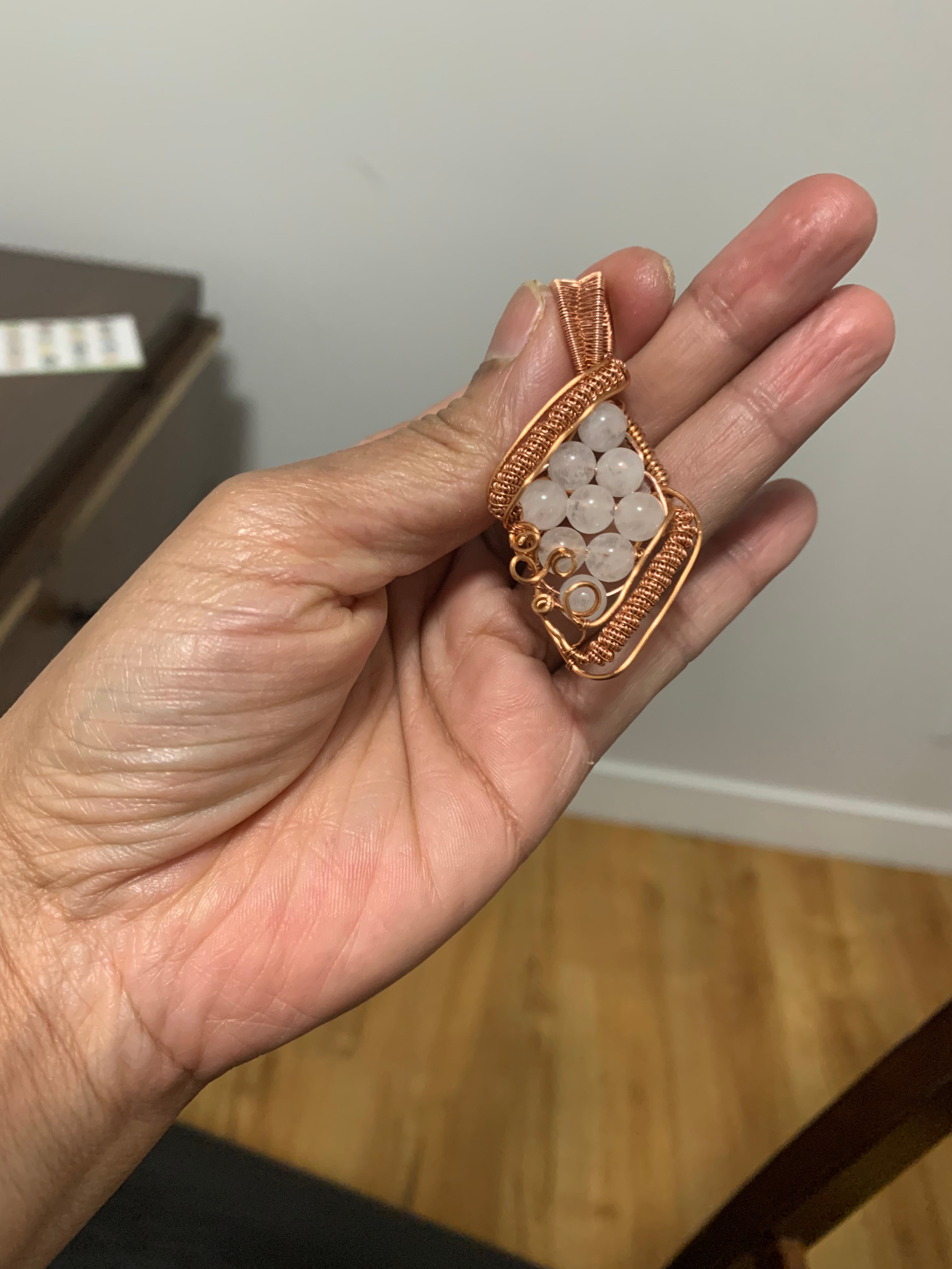 Close-up of handcrafted Morning Dew white jade copper wire wrapped pendant resting in a hand.