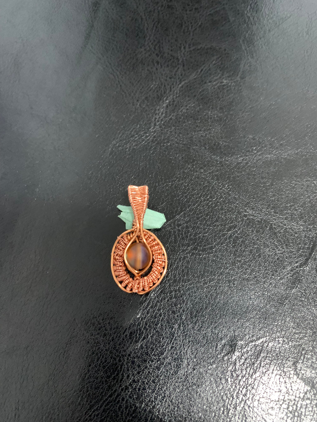 Copper pendant with a central mystic aura quartz on a dark textured surface