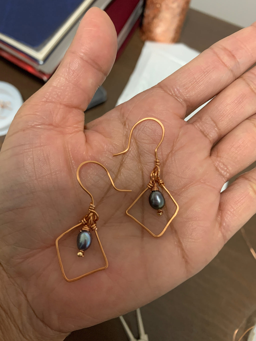 Pearl Alchemy geometric dangle earrings featuring dark grey pearls suspended within diamond-shaped copper wire frames.