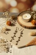 Handmade Pyrite Bloom copper earrings with pyrite gemstones arranged beside dried botanicals and candlelight.
