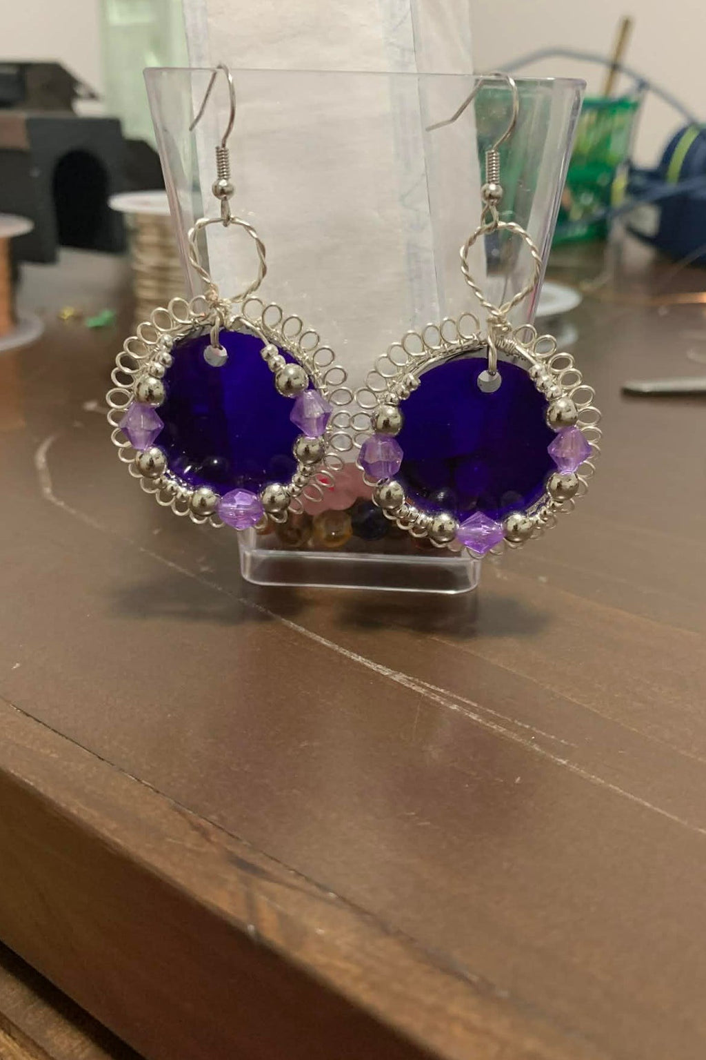 Pair of purple earrings on a clear stand with a blurred background