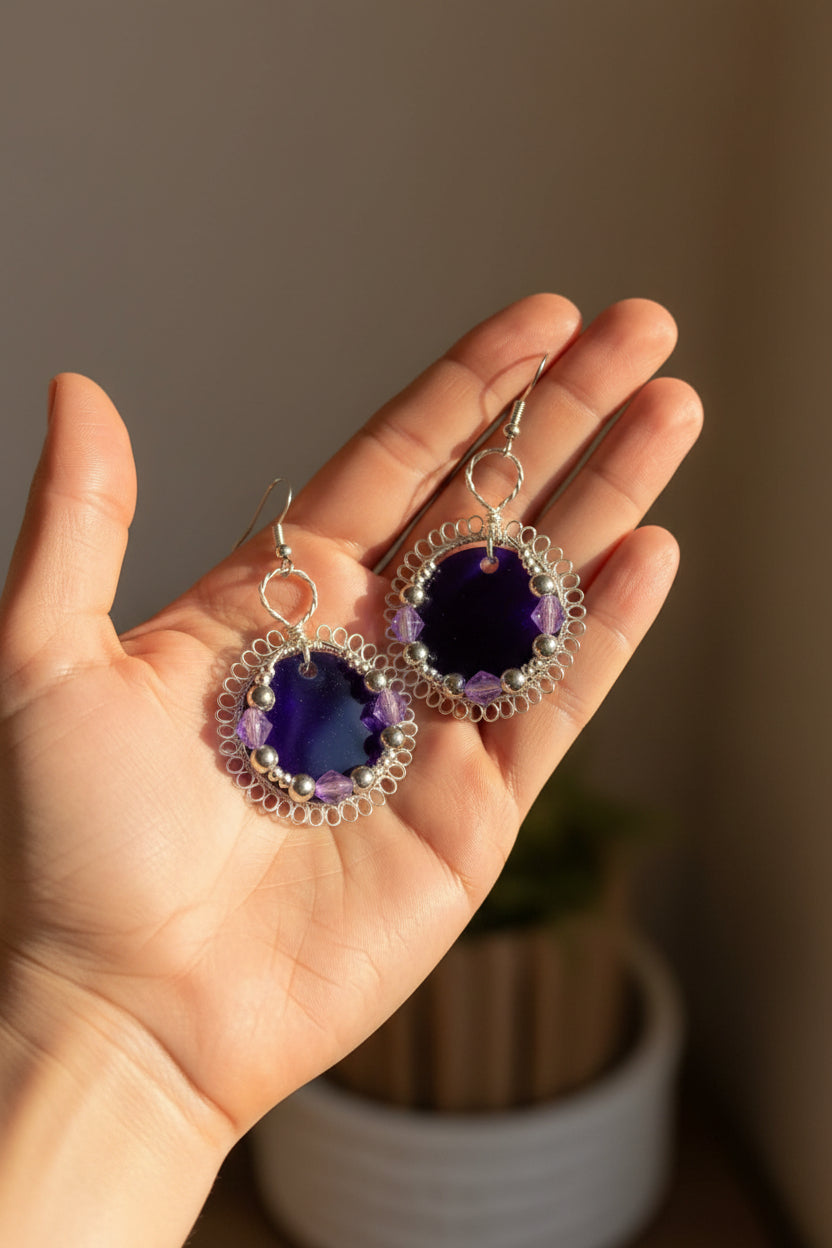 Hand holding handmade purple resin statement earrings showing size and intricate wire details.